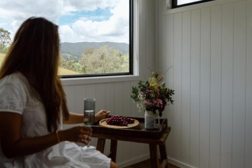 a woman sitting in front of a table with a cake at Luxe Farmstay, Main House and Brand New Tiny Home, Animals and Views! in Obi Obi