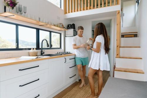a man and a woman standing in a kitchen at Luxe Farmstay, Main House and Brand New Tiny Home, Animals and Views! in Obi Obi