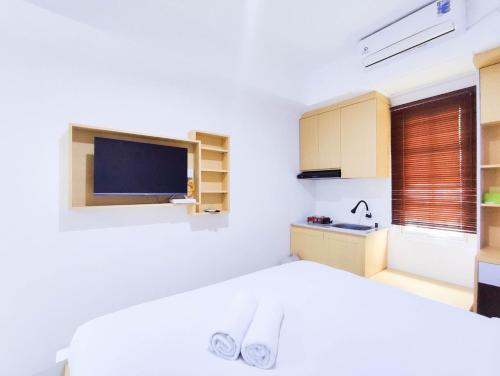 a white bedroom with a bed and a tv at Cozy Studio at 9th Floor Paltrow City Apartment By Travelio in Semarang
