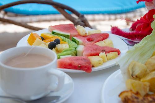 a table with two plates of fruit and a cup of coffee at Equalia Rose Hotel in Jambiani