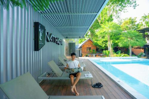 a man sitting on a chair next to a swimming pool at Natthapon Resort Kaeng Kachan in Kaeng Krachan