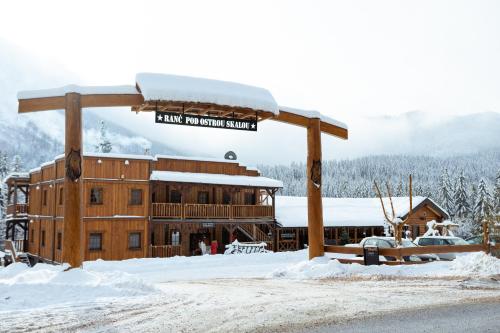 a large wooden building with a sign on it in the snow at Ranč pod Ostrou Skalou in Stratená