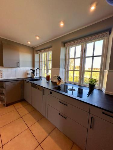 a large kitchen with white cabinets and black counter tops at Seesucht-Föhr - Moderne Reet-Haushälfte mit Sauna, Garten & Terrasse nahe Wattenmeer in Utersum