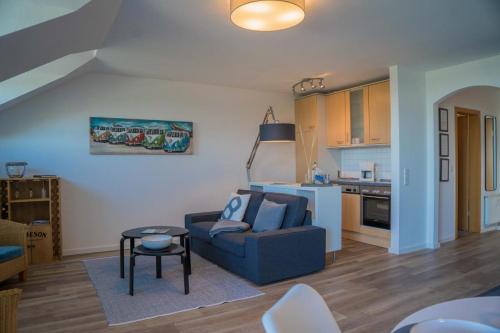 a living room with a blue couch and a kitchen at Inselblume 78 - Ferienwohnung mit Strandkorb in Burgtiefe in Burgtiefe auf Fehmarn 