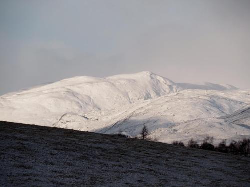 a snow covered hill with a mountain in the background at Jacobite Lodge by The House of Danu in Kingussie