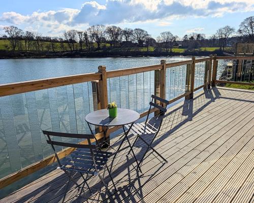 a table and two chairs on a deck next to the water at Otter's Pool Studio Apartment at Galwad Y Mor in Saint Dogmaels