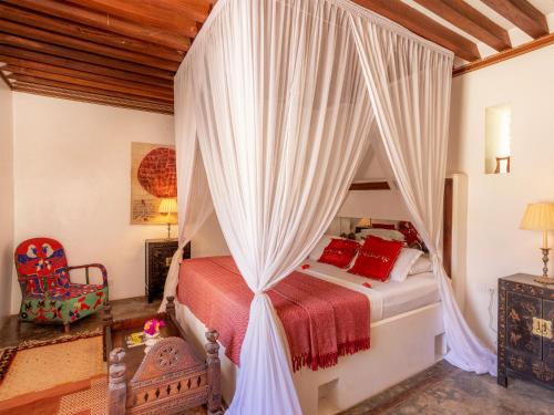 a bedroom with a canopy bed with red pillows at Dhow House in Shela