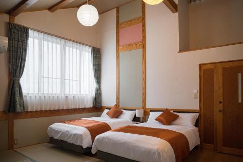 two beds in a room with a window at Cottage Roots コテージルーツ in Hida