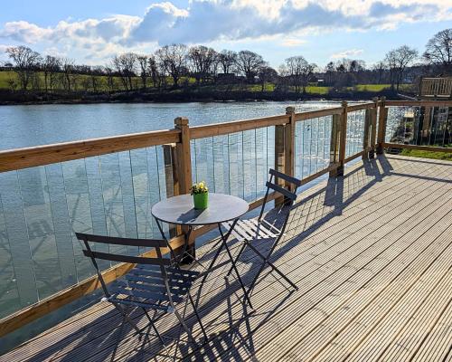 a table and two chairs on a deck next to the water at Otter's Pool Studio Apartment at Galwad Y Mor in Saint Dogmaels