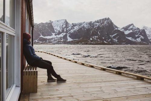 a man sitting on a deck looking out at the water at Eliassen Rorbuer in Reine