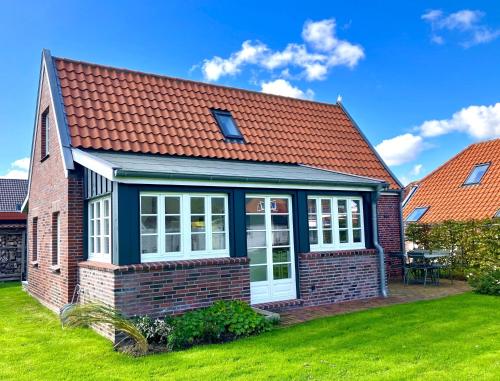 una casa con techo rojo y patio verde en Haus Lüsthuuske, en Dornum