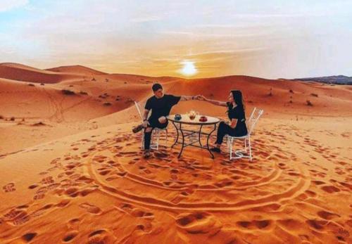 a man and woman sitting at a table in the desert at Merzouga Sara Luxury Camp in Merzouga