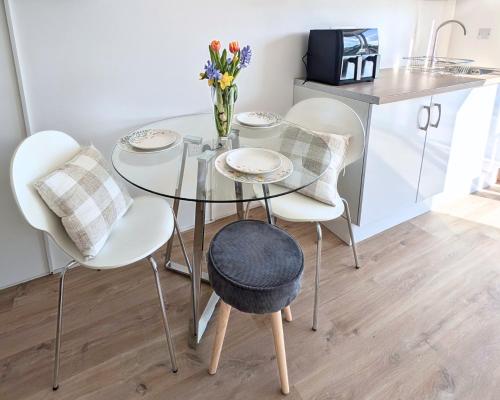 a glass table with white chairs and a vase of flowers at Otter's Pool Studio Apartment at Galwad Y Mor in Saint Dogmaels