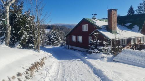 a red house in the snow with a snow covered driveway at Penzion V Kopci in Kořenov
