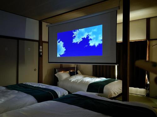 a large screen in a hotel room with two beds at 民宿ひだまり Minsyuku Hidamari in Kurashiki
