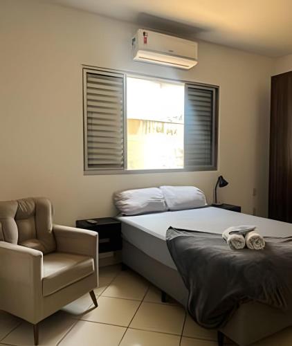 a bedroom with a bed and a chair and a window at Residencial Vicente Vaz in Patos de Minas