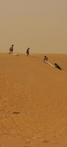 a group of people riding on surfboards in the desert at Les jardins fleuris de lompoul sur mer in Tioukougne Peul