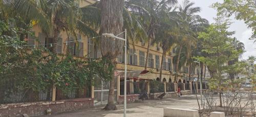 a yellow building with palm trees next to a street at Les jardins fleuris de lompoul sur mer in Tioukougne Peul
