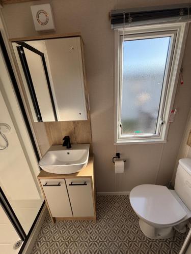 a bathroom with a sink and a toilet and a window at The Retreat 10 - Hot tub Mini Lodge, central heating, bed linen, & pet friendly - Meadow Lakes Caravan Hire in Chapel Saint Leonards