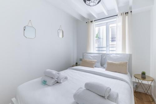 biała sypialnia z dużym białym łóżkiem z poduszkami w obiekcie Home Suite Home Grands Boulevards 41 w Paryżu