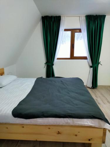 a bedroom with a bed with green curtains and a window at Cabanele A-nuc-A in Dăneşti