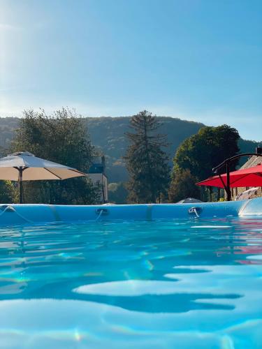 - une piscine d'eau bleue avec des parasols dans l'établissement Gîte Basilic Havre de Paix pour 7 Personnes au Cœur de la Nature et près de la Meuse, à Vireux-Wallerand