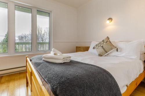 a bedroom with a bed with white sheets and windows at Chalet Entre Ciel et Fleuve, SPA, 5 CH, 5 SDB in Petite-Rivière-Saint-François