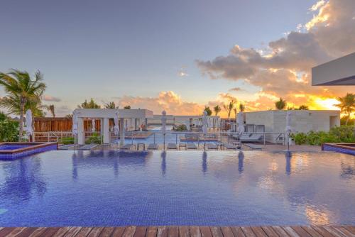 a large swimming pool with a sunset in the background at La Amada Residences Private Beach Getaway with Pools & Gym in Cancún