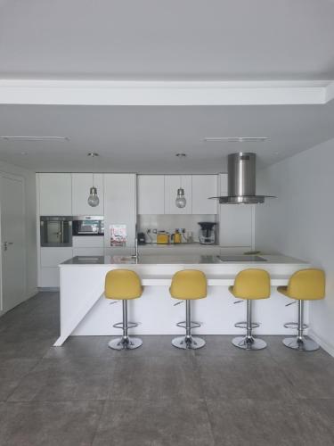 une cuisine avec des placards blancs et des tabourets de bar jaunes dans l'établissement Magnifique appartement - St Martin de Peille, à Peille