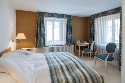 a bedroom with a bed and a desk and two windows at Hotel Post in Bivio