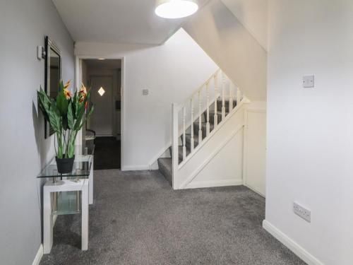 a white hallway with stairs and a vase of flowers on a table at Cheshire House in Castleton