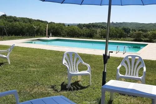 - deux chaises blanches et un parasol à côté de la piscine dans l'établissement Maison familiale avec piscine à Salviac, à Salviac
