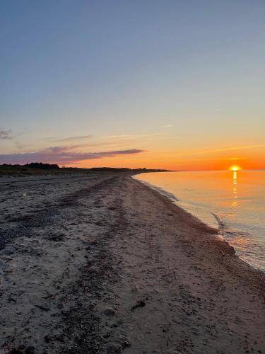 a beach with the sun setting over the water at Seaside holiday home in Grenå