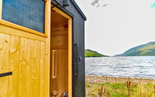 a wooden cabin next to a body of water at Otter Hostel Connemara in Leenaun