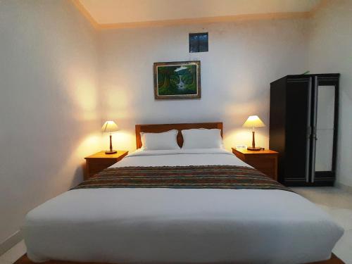 a bedroom with a large white bed with two lamps at Pondok Dauh Ancak Kelating Guest House in Krambitan