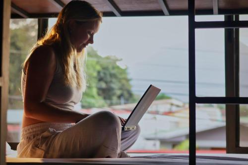 a woman sitting on the floor with a laptop at Ceiba Hostel in Fortuna