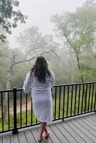 a woman in a white dress standing on a balcony at Firefly2 - luxury lakeside treehouse with hot tub in Eureka Springs