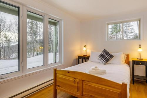 ein Schlafzimmer mit einem Bett mit weißen Laken und Fenstern in der Unterkunft Studio Entre Ciel et Fleuve in Petite-Rivière-Saint-François