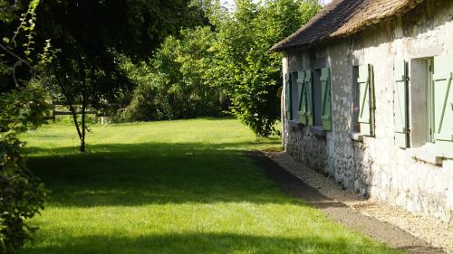 un ancien bâtiment en pierre avec une fenêtre verte et un champ dans l'établissement L'Allée - Maison d'hôtes - Charme - Digital detox, à Vernantes