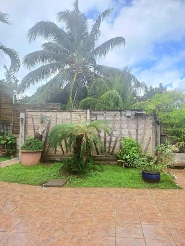a wooden fence with palm trees in a yard at Studio tout équipé et fonctionnel in Rivière-Salée