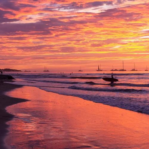 a person with a surfboard in the ocean at sunset at Casa Cocobolo Studio #1 in Tamarindo