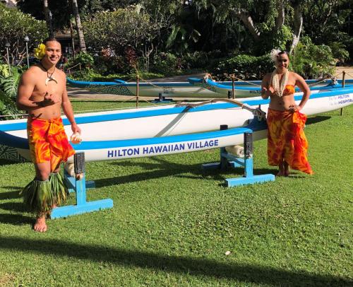 two men standing next to a boat on the grass at Hilton Hawaiian Village Waikiki Beach Resort in Honolulu