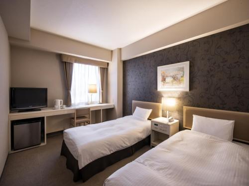 a hotel room with two beds and a desk at Business Inn Norte in Sapporo