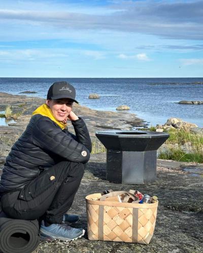 a woman kneeling next to a grill next to the ocean at Kustvy - En Destination intill Havet in Skärplinge