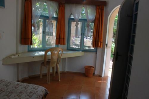 a bedroom with a table and two chairs and windows at New Creation Guest House in Auroville