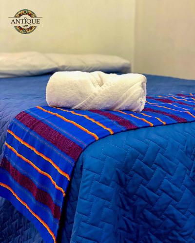 a bed with a blue and red quilt and two towels at Hostal Antique Luna in Santa Ana