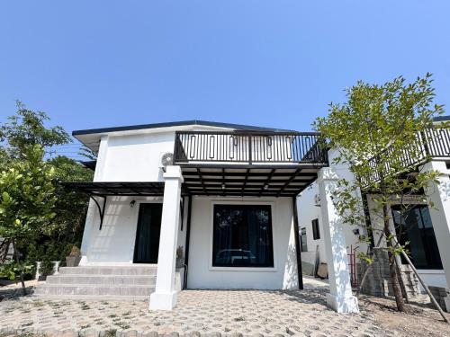 a white house with a balcony and stairs at Chiangmai Courtyard Residence บ้านสวนสวย บ้านถวาย in Bān Sawan