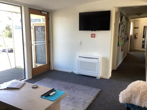 a living room with a table and a tv on a wall at Stay in School by the Sea in Dunedin
