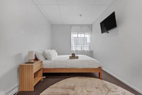 a white bedroom with a bed and a television at Onehunga Suites in Auckland