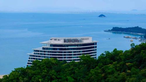 a tall building on top of a hill next to the water at Grand Ocean View Hotel Zhuhai in Zhuhai